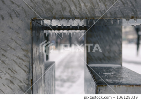 Winter urban decay. Chilly urban scene highlighting decayed metal and icy features. Cold winter scene showcasing weathered frame amidst snow and blurred city background 136129339