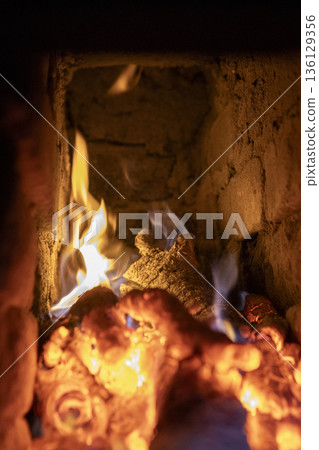 A fireplace with blazing wood. An antique brick hearth for warming the room. A fireplace with blazing wood. An antique brick hearth for warming the room. 136129356