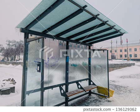 An ice-covered glass bus stop with an empty bench in the city An ice-covered glass bus stop with an empty bench in the city 136129362