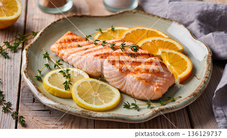 Grilled salmon fillet served with fresh lemon and orange slices on rustic ceramic plate, garnished with thyme, top view 136129737