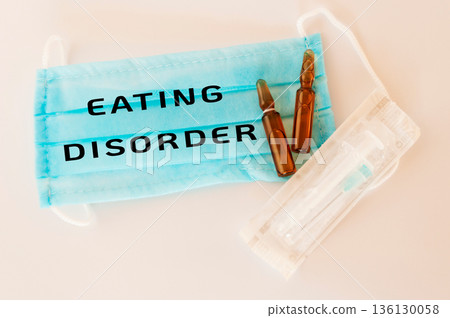 Medical mask with text about eating disorder, syringes, and vials on a clean surface Medical mask with text about eating disorder, syringes, and vials on a clean surface 136130058