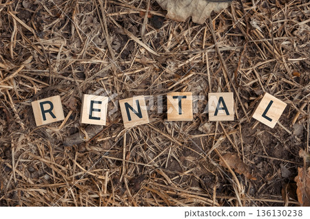 Wooden letter tiles spelling rental on a textured ground of dry grass and leaves Wooden letter tiles spelling rental on a textured ground of dry grass and leaves 136130238