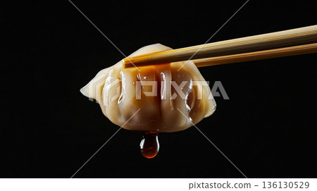 Dumpling held by chopsticks dripping with sauce against a dark background showcasing culinary art Dumpling held by chopsticks dripping with sauce against a dark background showcasing culinary art 136130529