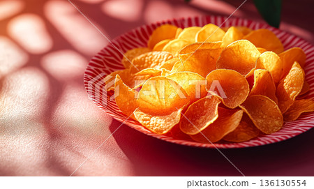 Crispy potato chips arranged in a vibrant bowl with soft shadows and warm lighting effects 136130554