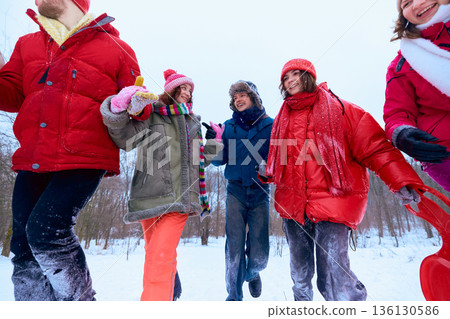 Friends walking together through snowy park smiling and talking. 136130586