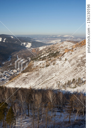 Scenic winter landscape with snow-covered mountains, bare trees, and a distant town under a clear blue sky, evoking a serene natural beauty. Scenic winter landscape with snow-covered mountains, bare trees, and a distant town under a clear blue sky, evoking a serene natural beauty. 136130596