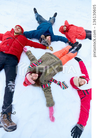 Group of friends lying in snow after winter sledding laughing together. 136130605