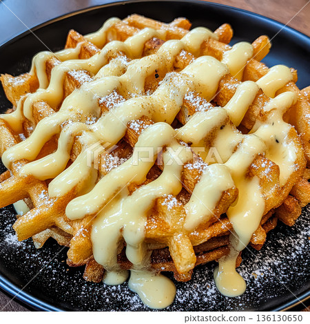 Plate of waffles covered in a creamy sauce and powdered sugar 136130650