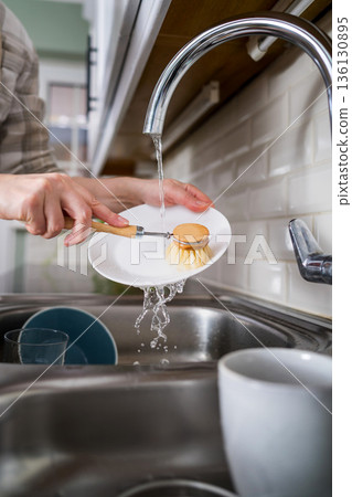 Washing dishes. Eco-friendly kitchen wooden brush. Woman washing dishes with bamboo brush. Waste-free, eco-friendly concept 136130895