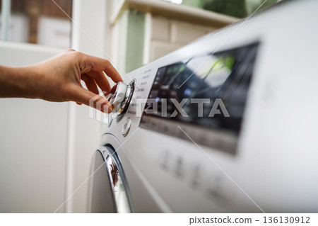 Smart home appliances. Adjusting washing machine setting. Hand turning the dial of a modern washing machine. Daily chores, copy space Smart home appliances. Adjusting washing machine setting. Hand turning the dial of a modern washing machine. Daily chores, copy space 136130912