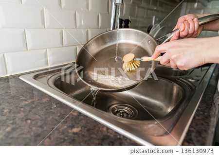 Woman washing a frying pan in the kitchen with eco friendly wooden brush for sustainable lifestyle Woman washing a frying pan in the kitchen with eco friendly wooden brush for sustainable lifestyle 136130973