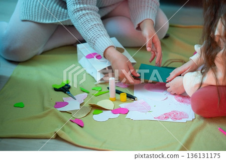 A mother and child create handmade cards together, crafting paper hearts and other shapes. A fun, creative bonding moment. 136131175