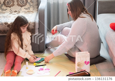 A woman and child create handmade crafts together, enjoying a heartwarming activity filled with creativity and bonding. A woman and child create handmade crafts together, enjoying a heartwarming activity filled with creativity and bonding. 136131176