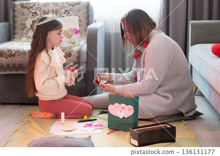 A girl and woman craft Valentine's Day gifts together, creating heart-shaped decorations and exchanging small presents. A moment of shared creativity and affection. 136131177