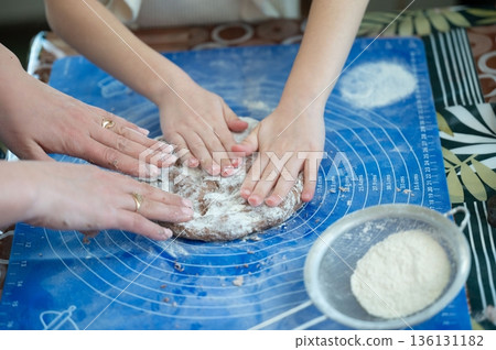 Hands gently shaping dough, a collaborative baking scene. Flour dusts the blue surface. A moment of shared creation. 136131182