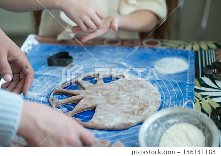 People prepare a dough for baking, using cookie cutters to create shapes. People prepare a dough for baking, using cookie cutters to create shapes. 136131183