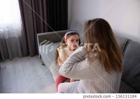 A young girl sits on a couch, engaging in a quiet moment with a woman. Their interaction is intimate and full of warmth. A young girl sits on a couch, engaging in a quiet moment with a woman. Their interaction is intimate and full of warmth. 136131184