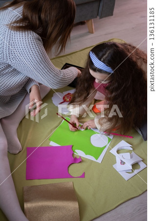 A mother and daughter engage in a creative crafting session, meticulously working with colorful paper and stencils. A mother and daughter engage in a creative crafting session, meticulously working with colorful paper and stencils. 136131185