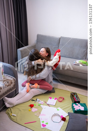 A heartwarming embrace between a mother and daughter, celebrating a special occasion with handmade cards and crafts. 136131187