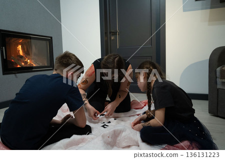 A woman and two children with temporary tattoos work together on a craft project by a fireplace. A woman and two children with temporary tattoos work together on a craft project by a fireplace. 136131223