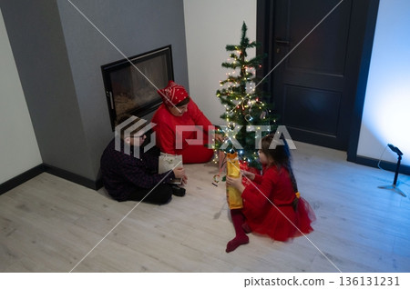 Christmas morning joy. A grandmother and two grandchildren exchange gifts by a decorated tree. 136131231
