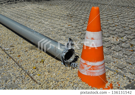 A broken streetlight pole on the ground in an urban area, marked by an orange traffic cone for safety. Concept: public safety, road hazards, city services, and urban restoration. 136131542