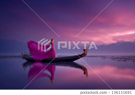A beautiful woman in a luminous glowing pink dress sails a boat on a vast lake at dusk A beautiful woman in a luminous glowing pink dress sails a boat on a vast lake at dusk 136131691