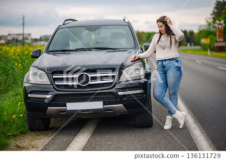 Woman standing next to her luxury black SUV on the side of a rural highway 136131729