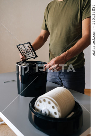 Vertical cropped shot of unrecognizable man holding air humidifier filter, cleaning and maintaining optimal humidity levels in home, promoting clean, fresh air for healthier living environment. 136132853