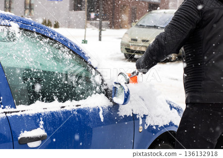 Individual in gloves brushing snow from vehicle on frosty residential street under gray sky Individual in gloves brushing snow from vehicle on frosty residential street under gray sky 136132918