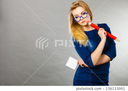 Confused woman holds big pencil note paper in hand Confused woman holds big pencil note paper in hand 136133001