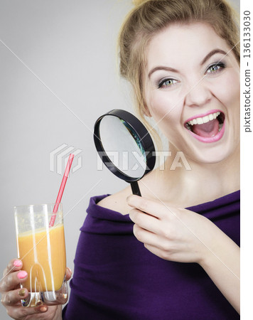 Woman holding magnifying glass investigating juice 136133030