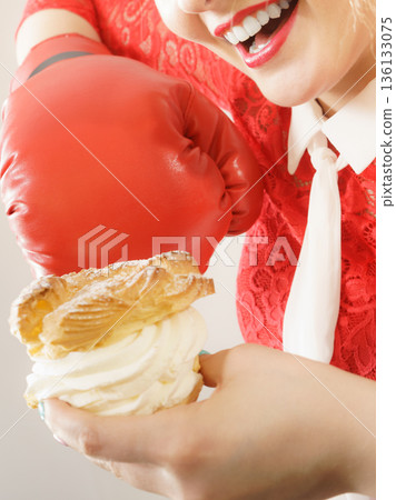 Woman fighting off bad food, boxing cream puff cake Woman fighting off bad food, boxing cream puff cake 136133075