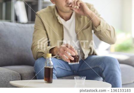 Man with alcohol addiction holding whiskey and cigarette at home, health risk Man with alcohol addiction holding whiskey and cigarette at home, health risk 136133183