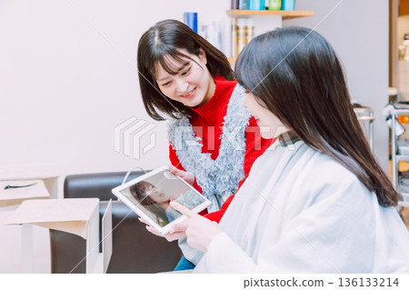 A hairdresser showing a tablet to a female customer at a beauty salon 136133214