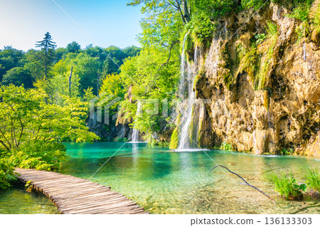 Wooden footpath at Plitvice national park, Croatia. Pathway in the forest near the lake and waterfall. Fresh beautiful nature, peaceful place. Famous tourist destination. Wooden footpath at Plitvice national park, Croatia. Pathway in the forest near the lake and waterfall. Fresh beautiful nature, peaceful place. Famous tourist destination. 136133303
