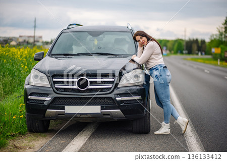 Woman driver pausing during road trip on highway, leaning on SUV, springtime traveling Woman driver pausing during road trip on highway, leaning on SUV, springtime traveling 136133412