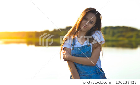 Young woman enjoying summer sunset at the lake, embracing peaceful nature Young woman enjoying summer sunset at the lake, embracing peaceful nature 136133425