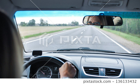 Woman driving car on open road, looking in rearview mirror, traveling concept Woman driving car on open road, looking in rearview mirror, traveling concept 136133432