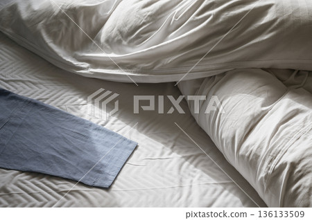 Morning light on unmade bed with blue cloth 136133509