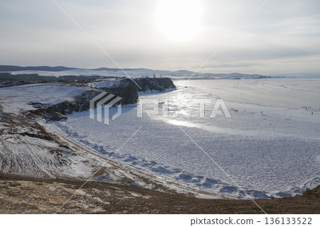 Khuzir, Olkhon Island: Wide winter view of the frozen surface of Lake Baikal with snow-covered shoreline, rocky cliffs, and distant hills 136133522