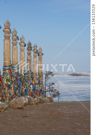 Colorful shamanic serge wooden poles adorned with prayer ribbons stand beside the frozen surface of Lake Baikal, capturing cultural tradition Colorful shamanic serge wooden poles adorned with prayer ribbons stand beside the frozen surface of Lake Baikal, capturing cultural tradition 136133529