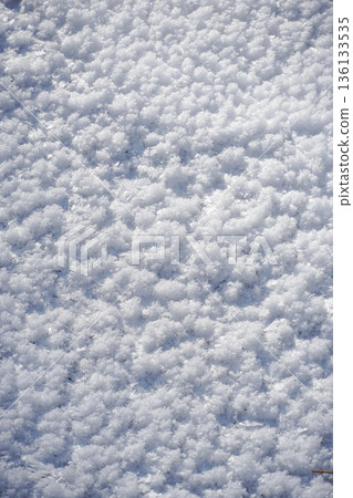 Dense white ice crystals form a soft textured surface, creating an abstract winter pattern with subtle light and shadow 136133535