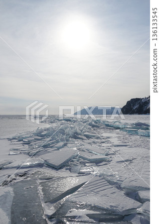 Broken ice plates and translucent shards spread across the frozen surface of Lake Baikal under low winter sun and pale sky Broken ice plates and translucent shards spread across the frozen surface of Lake Baikal under low winter sun and pale sky 136133545