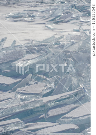 Sharp translucent ice plates, turquoise shards form dramatic frozen patterns on the surface of Lake Baikal with distant mountains in soft winter light 136133548