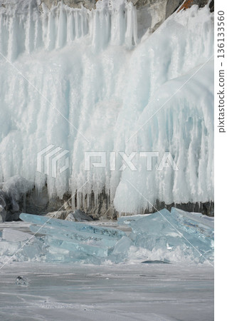 Sharp turquoise ice shards lie on the frozen surface of Lake Baikal with massive ice-covered cliffs in the background under clear winter light Sharp turquoise ice shards lie on the frozen surface of Lake Baikal with massive ice-covered cliffs in the background under clear winter light 136133560