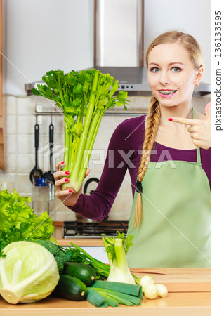 Woman in kitchen holds green celery Woman in kitchen holds green celery 136133595