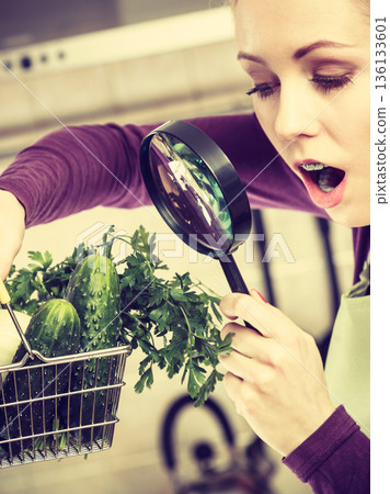 Woman looking through magnifier at vegetables basket 136133601