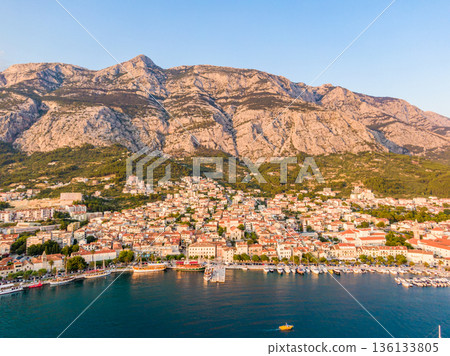 Drone aerial view of Makarska city, Croatia. Sunset over the city, beach and se. Biokovo mountains in the background. Summer time. Drone aerial view of Makarska city, Croatia. Sunset over the city, beach and se. Biokovo mountains in the background. Summer time. 136133805