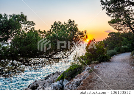 Sunset over the small path with grass, bushes and trees, near the Makarska city, Croatia. Sunset over the small path with grass, bushes and trees, near the Makarska city, Croatia. 136133832